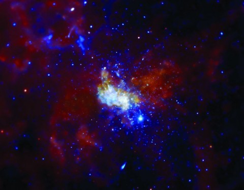 天の川銀河の心臓部にあるブラックホールを囲む荒々しい領域。エックス線はエネルギー量によって色分けされていて、赤が最も弱く、青になるほど強くなる。ブラックホールそのものは、明るい中心部分の一番上に横たわっていて、近隣にある巨星が放出した高温ガスの層の中に埋もれている。チャンドラX線観測衛星で撮影した画像。（NASA/CXC/MIT/F. Baganoff, R. Shcherbakov et al.）